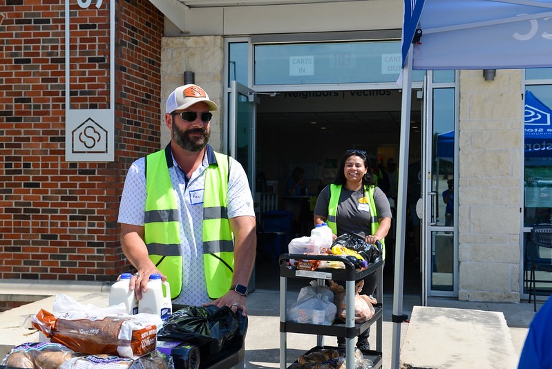 Two Dent Mechanic Group volunteers in yellow safety vests push carts of bread, milk, and grocery bags outside The Storehouse.